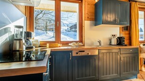 Une cuisine moderne avec des meubles de couleur sombre, une grande fenêtre et une vue sur un paysage enneigé.