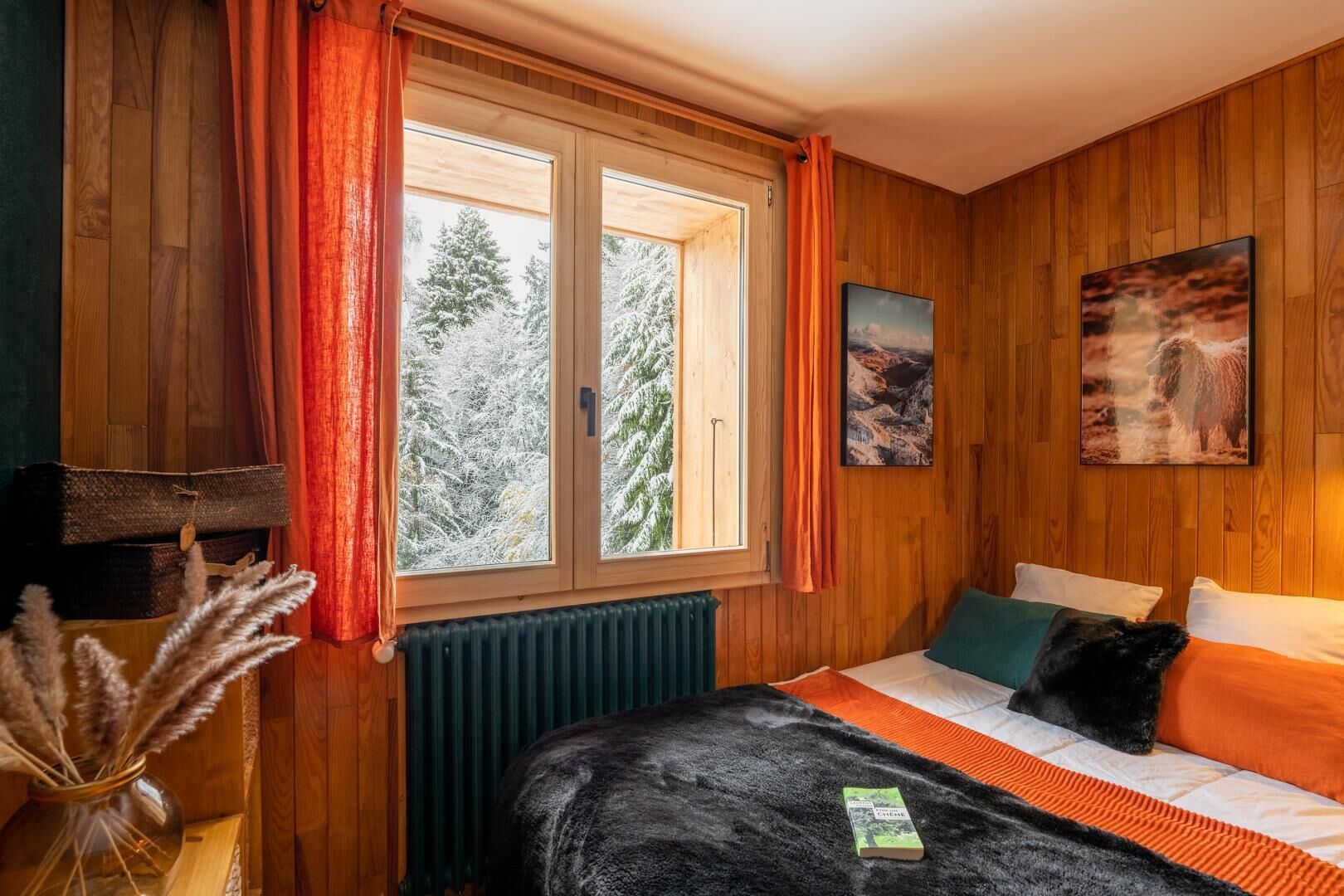 Une pièce confortable avec un lit, une fenêtre avec des rideaux, un radiateur et un tableau accroché au mur.