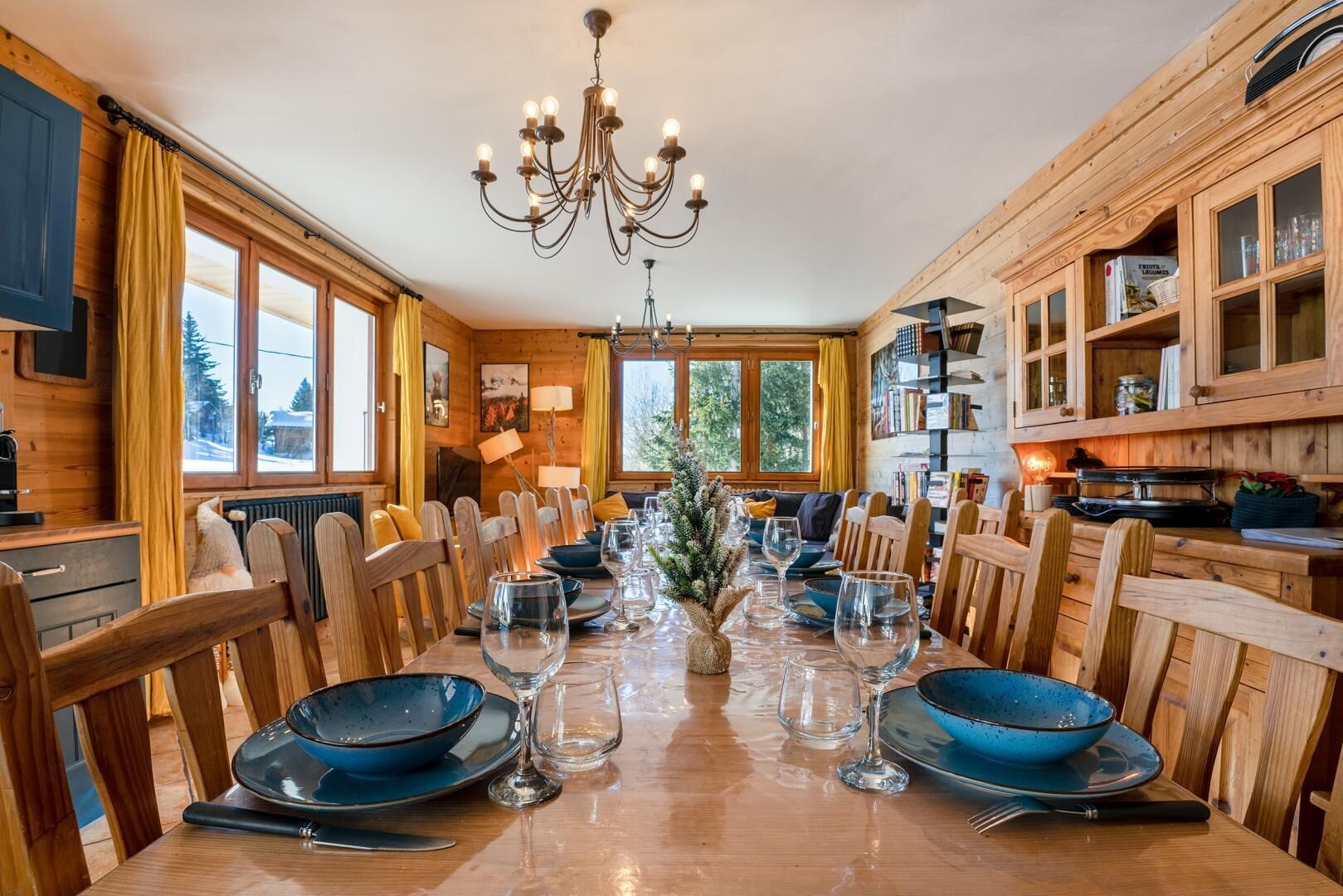 A wooden dining room with a long table set for a meal, surrounded by wooden chairs.