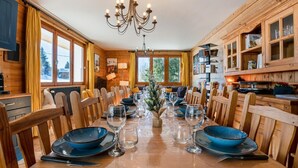 Une salle à manger en bois, avec une longue table dressée pour un repas, entourée de chaises en bois.