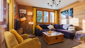Un salon confortable avec un canapé, des fauteuils, une table basse sur laquelle sont disposés des fruits et un téléviseur.