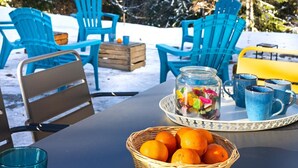Une table avec un panier d’oranges, un bocal de bonbons variés et des tasses bleues sur un plateau.