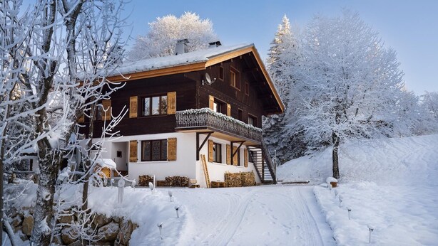 Un chalet en bois doté d’un balcon, entouré d’arbres couverts de neige.