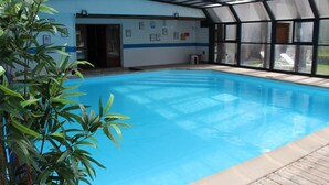 Una piscina interior con agua cristalina y azul, rodeada por una terraza de madera y paredes de vidrio.
