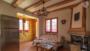 Una habitación acogedora con techo de madera, un sofá, una mesa con un libro, una chimenea y una ventana decorada con un corazón.