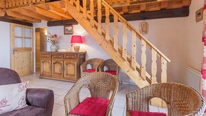 A wooden staircase leading to an upper floor, a wicker sofa with red cushions, a wooden cabinet with a vase and lamp, and a door with glass panels. - LES Diablotins - St-francois-longchamp (SAINT FRANCOIS LONGCHAMP)