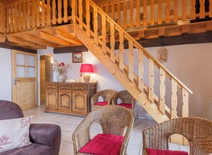 A wooden staircase leading to an upper floor, a wicker sofa with red cushions, a wooden cabinet with a vase and lamp, and a door with glass panels.