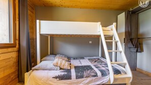 Una cama litera con escalera, una ventana con cortinas y una puerta con una toalla colgada.