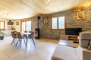 Un salon moderne avec un mur en pierre, un coin repas avec des chaises, un téléviseur et une cheminée.