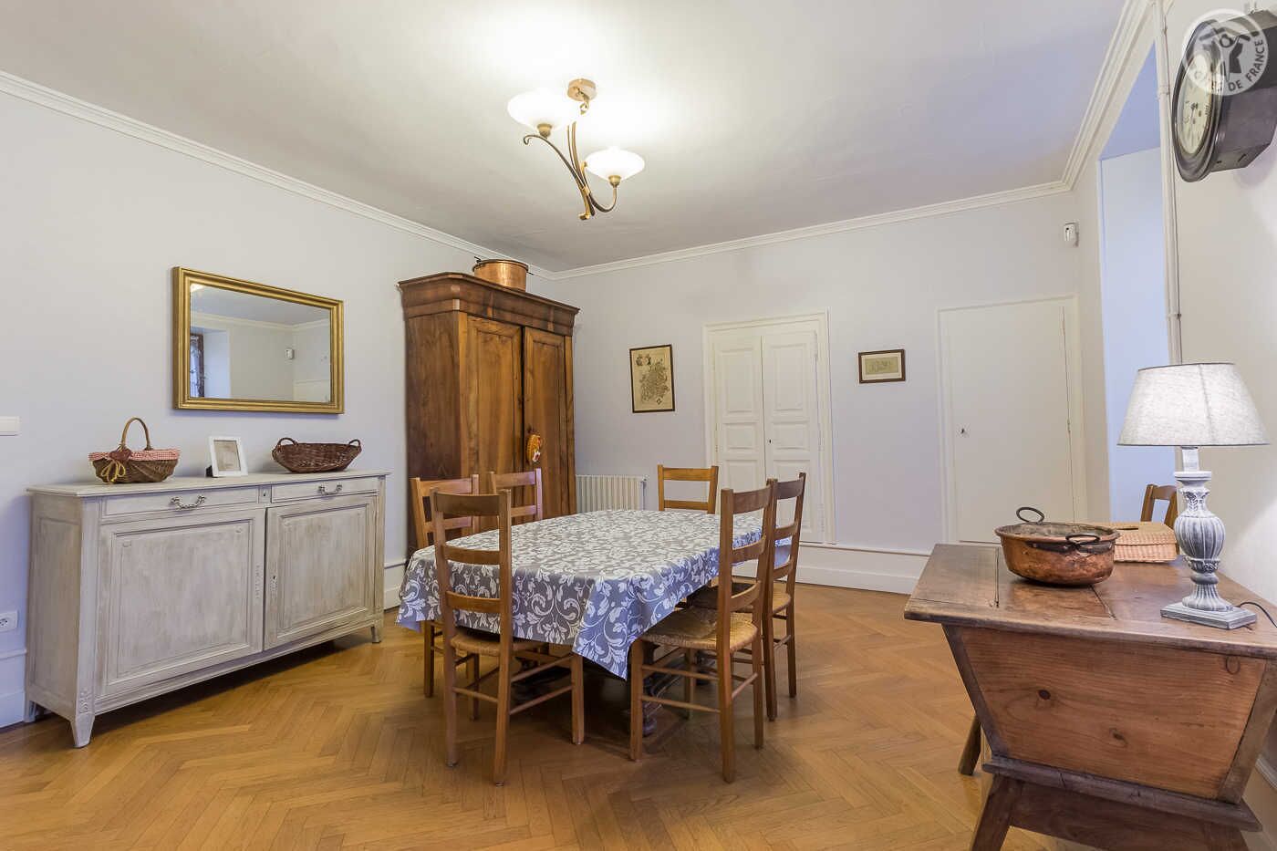 Un comedor con una mesa de madera, sillas, una araña, un aparador y un reloj en la pared.