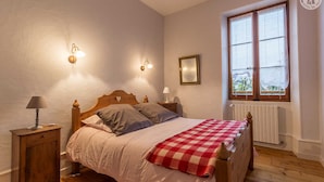 A bedroom with a wooden bed, two bedside lamps, a window with a view, and a radiator.