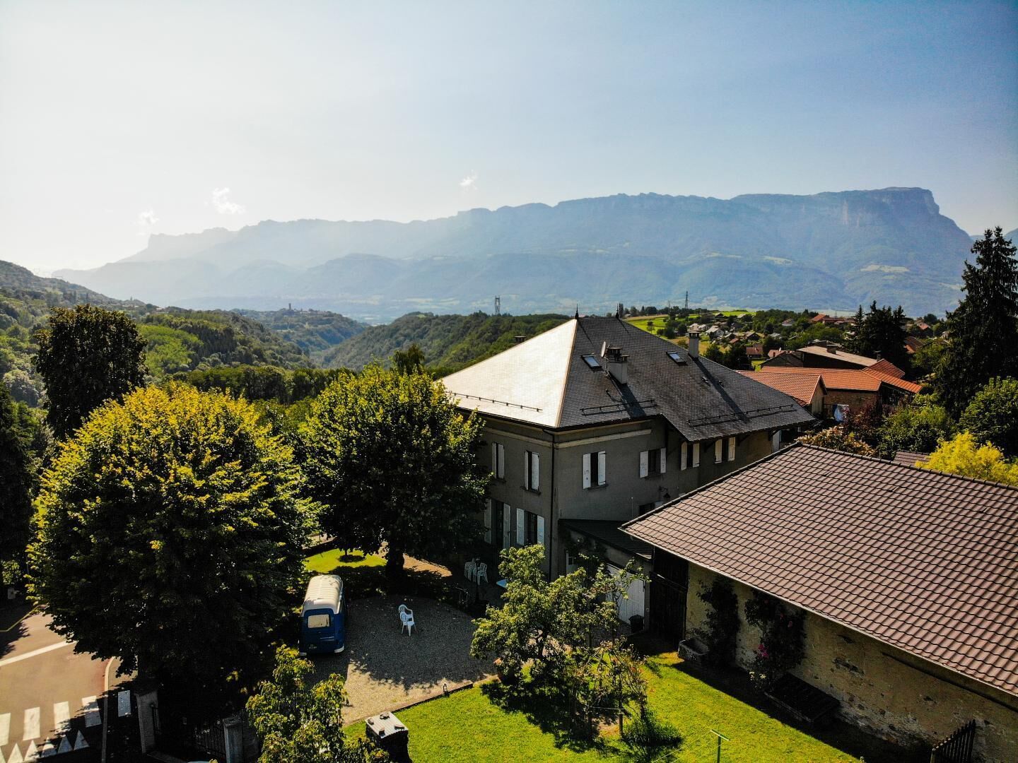 A residential building with a sloped roof, surrounded by lush greenery and a mountainous backdrop.