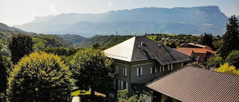 A residential building with a sloped roof, surrounded by lush greenery and a mountainous backdrop.