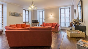 A living room with a large orange sofa, a television, and a chandelier.