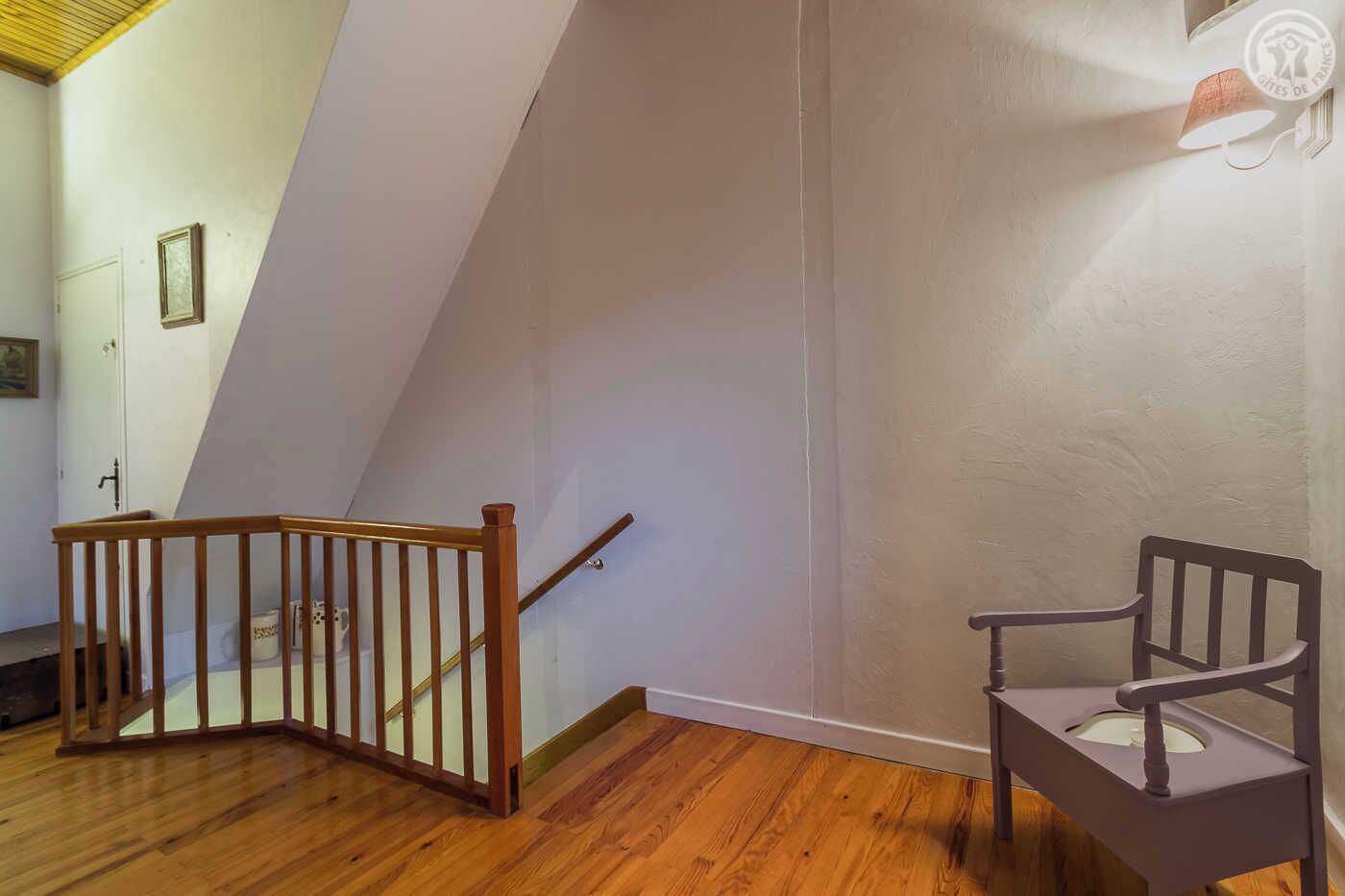 A room with a wooden staircase, a chair, and a wall-mounted light fixture.