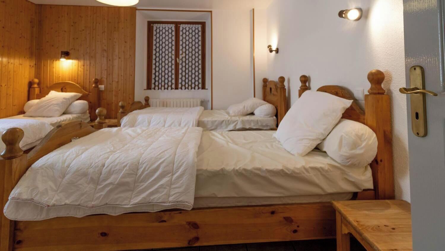 Ein Zimmer mit zwei Holzbettgestellen, jeweils mit Kopfseiten und einem Nachttisch, sowie einer Wandleuchte.