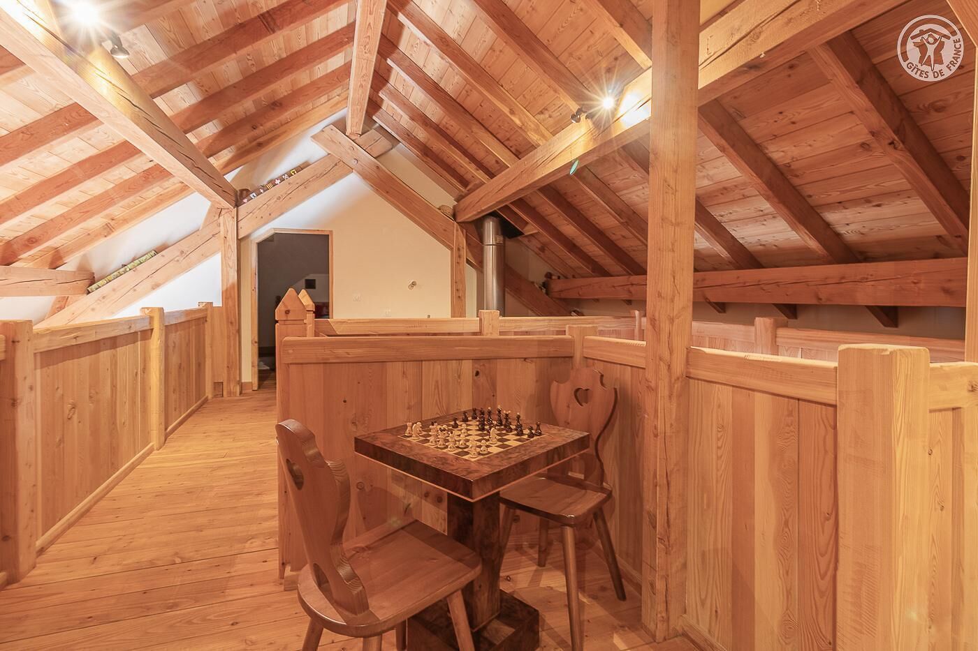A wooden loft room with a chessboard set up at a table, wooden benches, and a high ceiling with exposed beams.