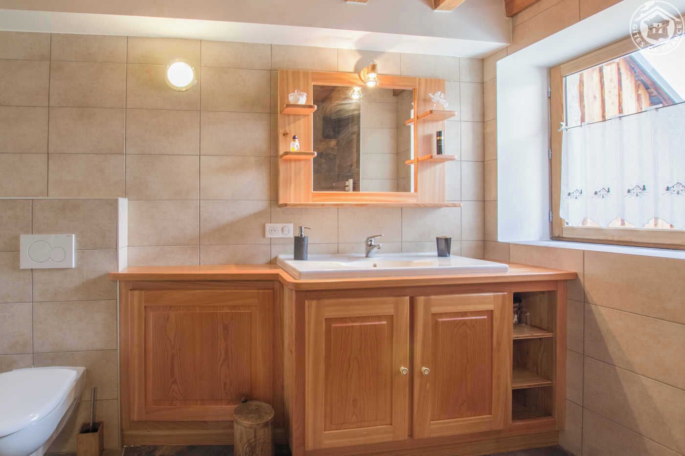 Un baño con tocador de madera, lavamanos y espejo.
