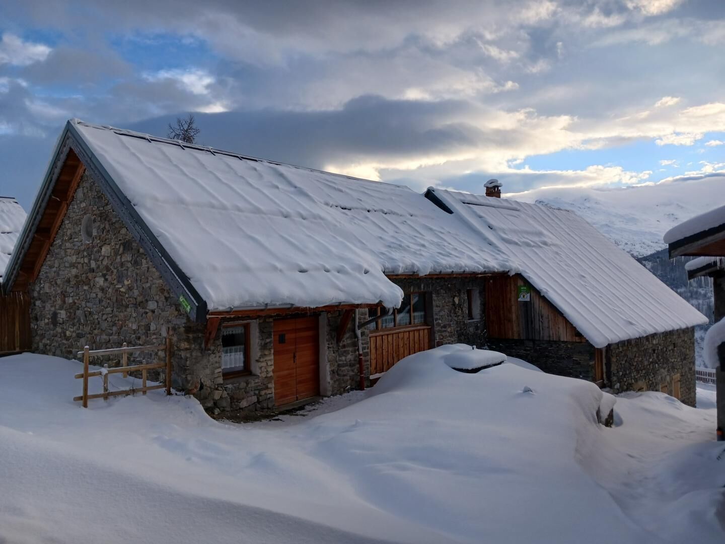 A stone building with a sloped roof covered in snow, wooden doors, and a wooden staircase leading to the entrance.