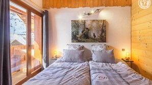A cozy bedroom with two beds, a large window with curtains, a painting above the beds, and wooden walls.