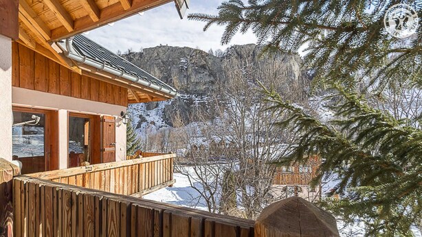 A wooden cabin with a balcony overlooking a snowy mountain landscape.