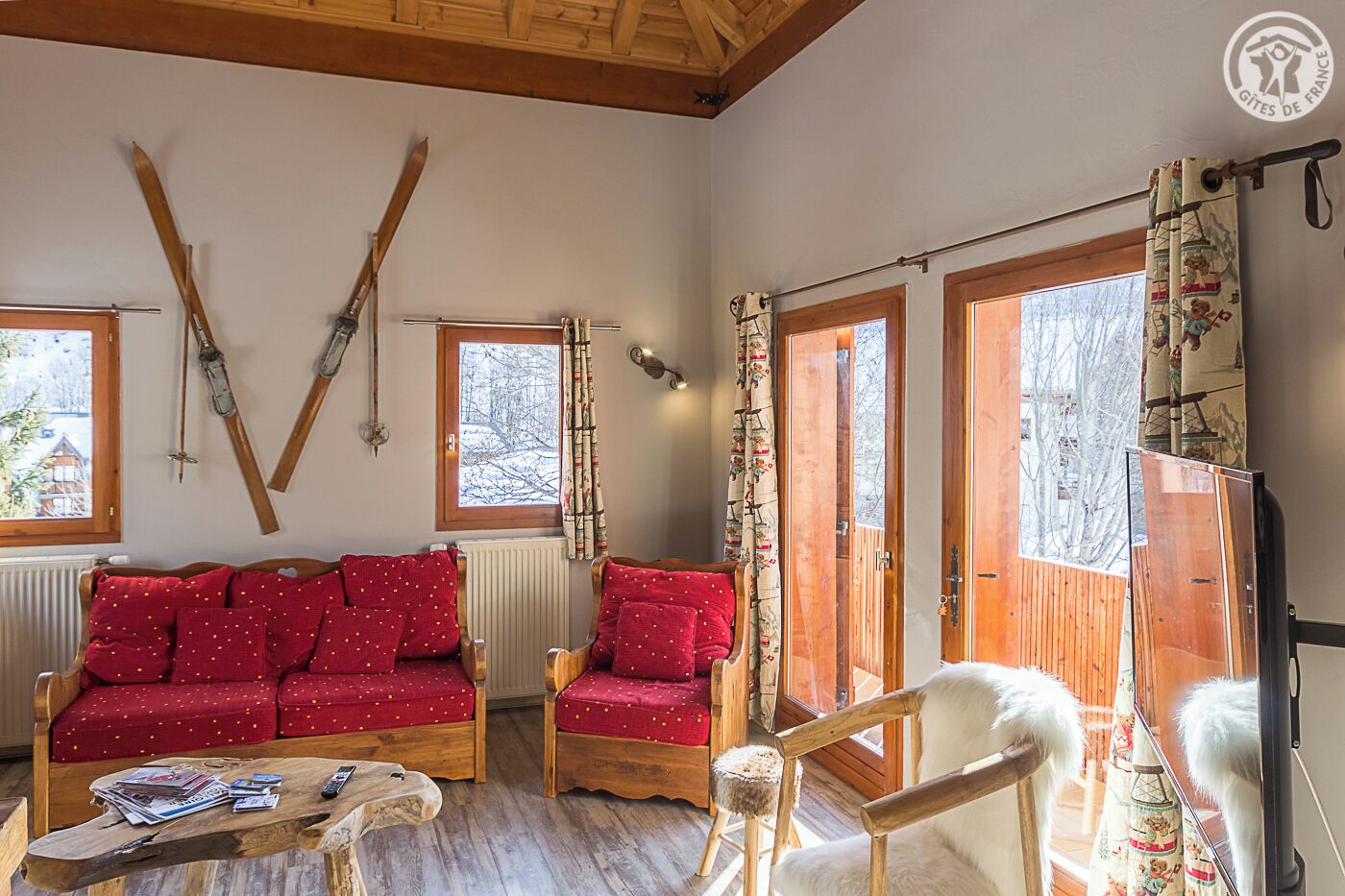 Une pièce chaleureuse avec un canapé rouge, des chaises en bois, une table basse en bois et des paires de skis accrochées au mur.