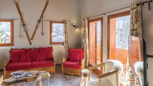 A cozy room with a red sofa, wooden chairs, a wooden coffee table, and skis hanging on the wall.