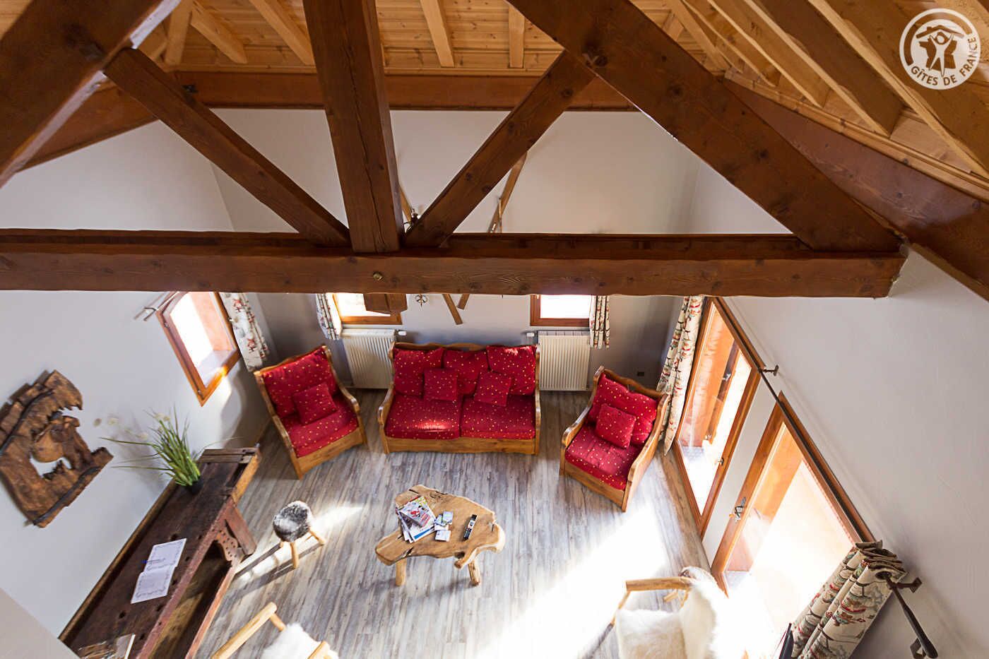 Une pièce chaleureuse avec un plafond en bois, un ensemble de canapés rouges, une table basse et une petite table sur laquelle se trouvent des livres et une bouteille.