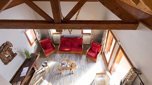 A cozy room with a wooden ceiling, a red sofa set, a coffee table, and a small table with books and a bottle.