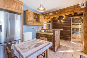 Uma cozinha rústica com armários de madeira, uma geladeira de aço inoxidável, uma mesa de jantar de madeira e uma lareira de pedra.