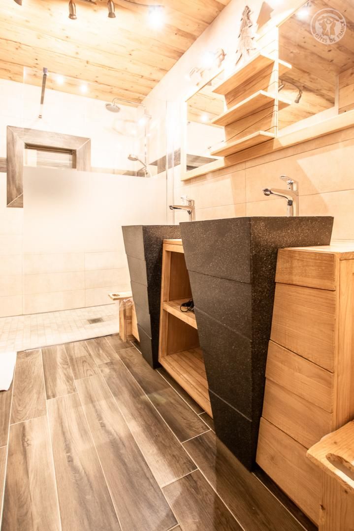Ein Holzinnenraum mit einem modernen Badezimmer, das eine Dusche, ein Waschbecken mit schwarzer Arbeitsplatte und eine Holzkabine beinhaltet.