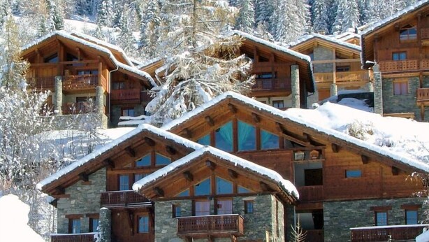 Eine mehrstöckige Lodge mit hölzernen Balkonen und Steinwänden, umgeben von schneebedeckten Bäumen.