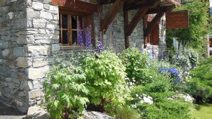Ein Steinhaus mit hölzernen Balkonen und einem Garten mit verschiedenen Pflanzen und Blumen.
