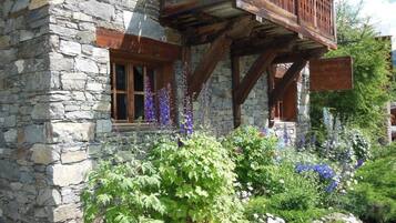 Un bâtiment en pierre doté de balcons en bois et d’un jardin où poussent diverses plantes et fleurs.