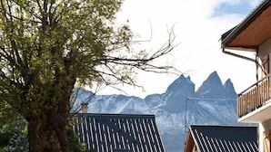 A building with a wooden facade, a large tree in the foreground, and a mountain range in the background.