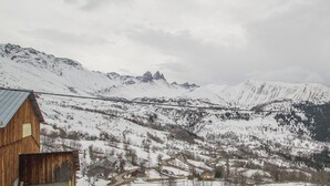 A wooden cabin with a metal roof, surrounded by snow-covered mountains and a cloudy sky.