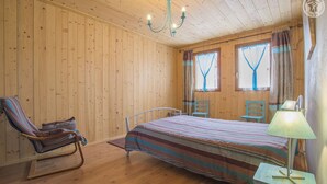 A wooden-paneled room with a bed, a rocking chair, and a small table with a lamp.