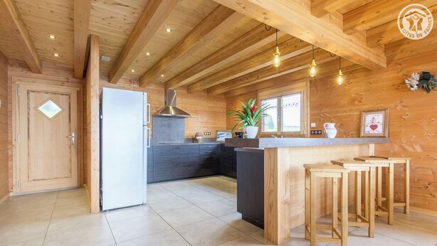 Una cocina moderna con vigas de madera, una isla central, taburetes de bar y un ventanal amplio.