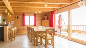 Un interior de madera con una mesa y sillas para comer, una zona de cocina y ventanas amplias con cortinas rojas.