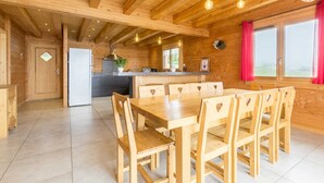 Interior de una cabaña de madera con comedor, cocina y un amplio ventanal con cortinas rojas.