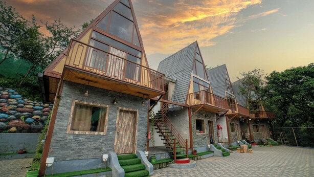 A row of modern, triangular-roofed cottages with balconies, a stone facade, and a paved courtyard. - Mudras Grove Resort (Nainital)