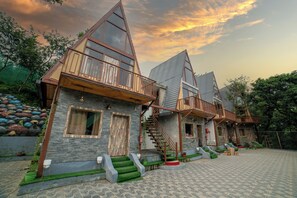 A row of modern, triangular-roofed cottages with balconies, a stone facade, and a paved courtyard. - Mudras Grove Resort (Nainital)