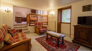 A living room with a sofa, a plaid armchair, a coffee table, a TV, and a staircase leading to a kitchen. - LES Mentens - Mouxy - Gîte (MOUXY)