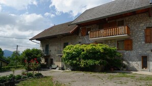 A stone building with a balcony, surrounded by greenery and a gravel driveway. - LES Mentens - Mouxy - Gîte (MOUXY)