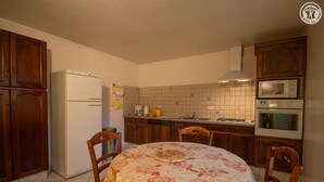 A compact kitchen with wooden cabinets, a refrigerator, a microwave, and a stove. There is a round table with chairs and a floral tablecloth. - LES Mentens - Mouxy - Gîte (MOUXY)