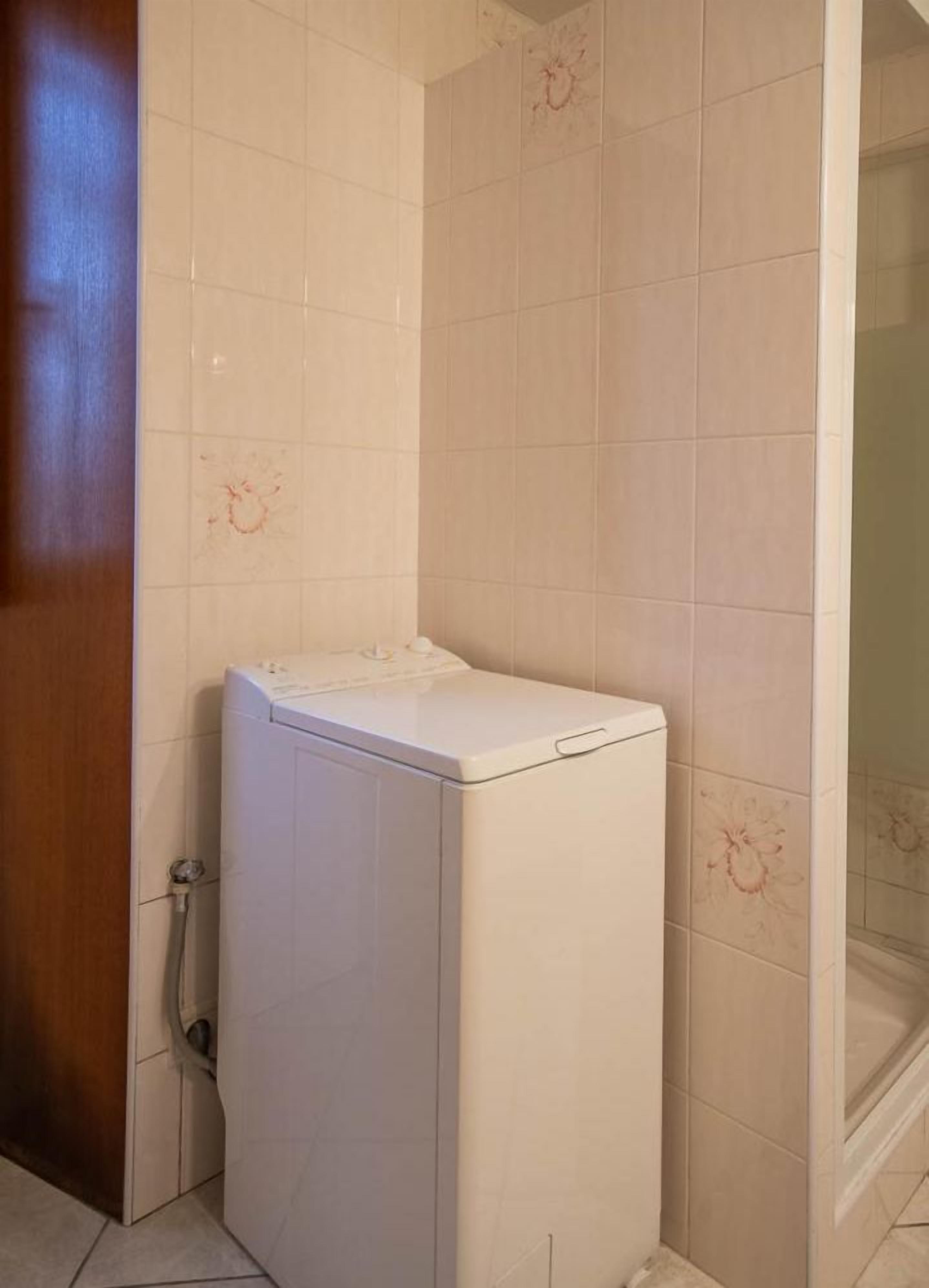 A compact room with a washing machine, a shower area, and a wooden door.