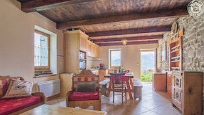 Un espacio acogedor con una mesa de madera, un sofá y una silla. Hay una cocina con armarios de madera y un ventanal.