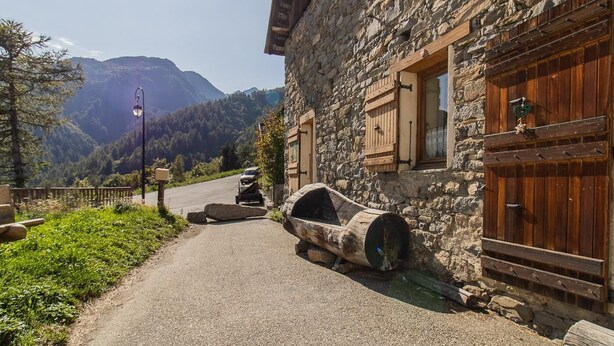 Un edificio de piedra con contraventanas de madera, un barril rústico y vistas a la montaña.