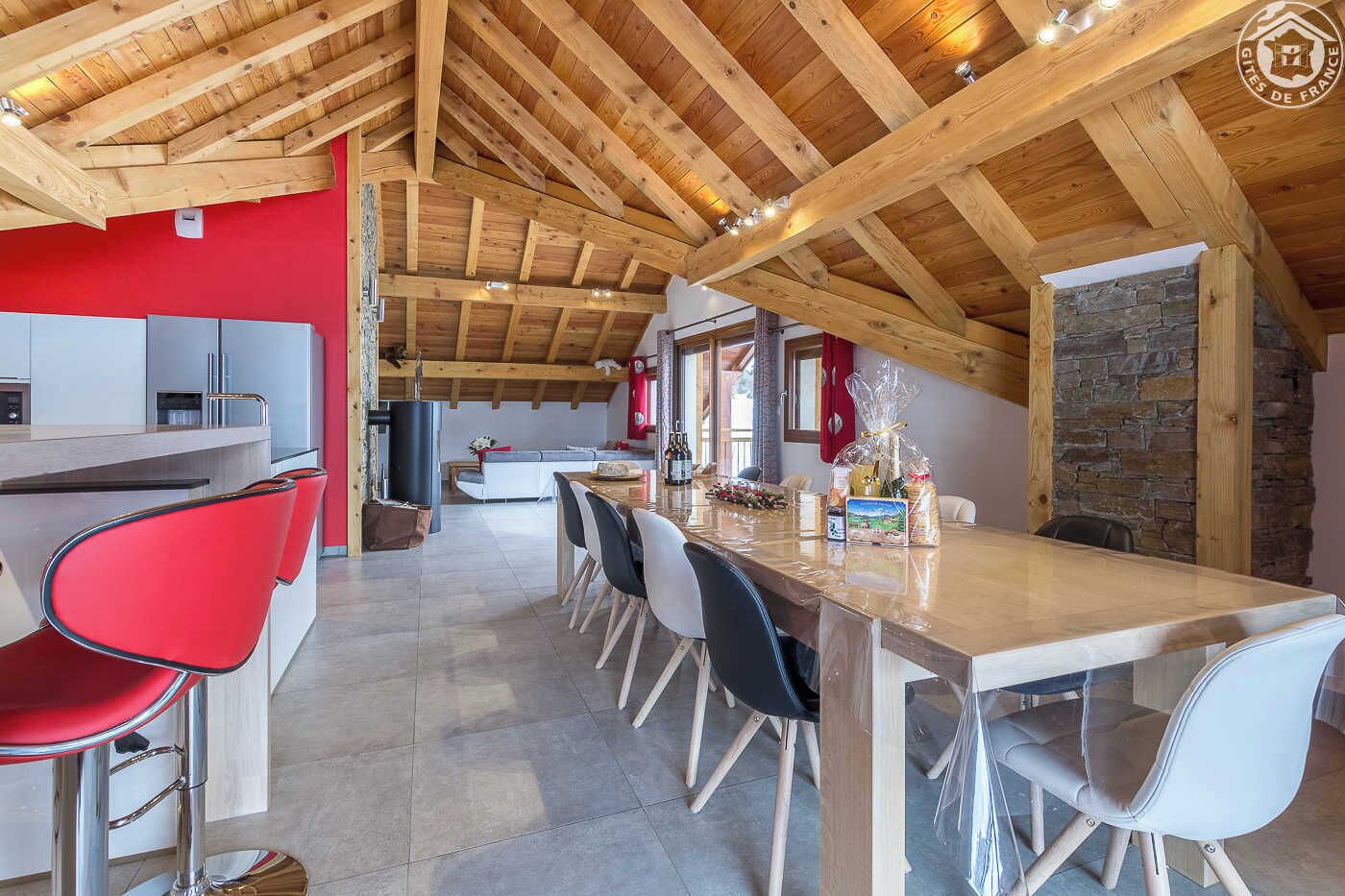 Une cuisine moderne avec un plafond en bois, un coin repas avec des chaises et un mur en pierre.