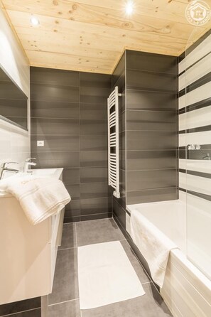 Een moderne badkamer met een houten plafond, een witte wastafel, een badkuip en een handdoekhouder.